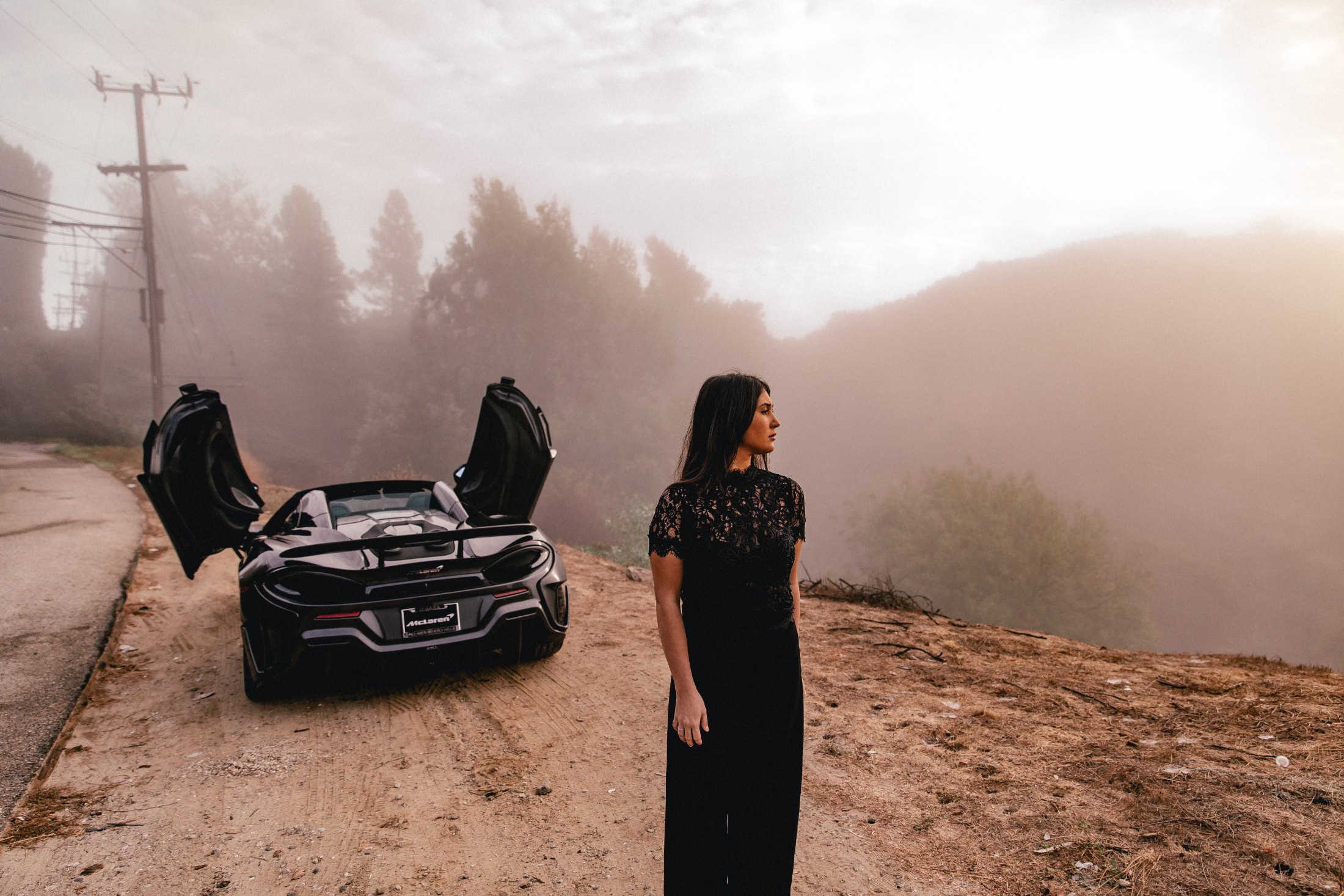McLaren 600LT Spider – woman in black beside the car with butterfly doors open, on a hillside road in the fog, photo Jon Filin