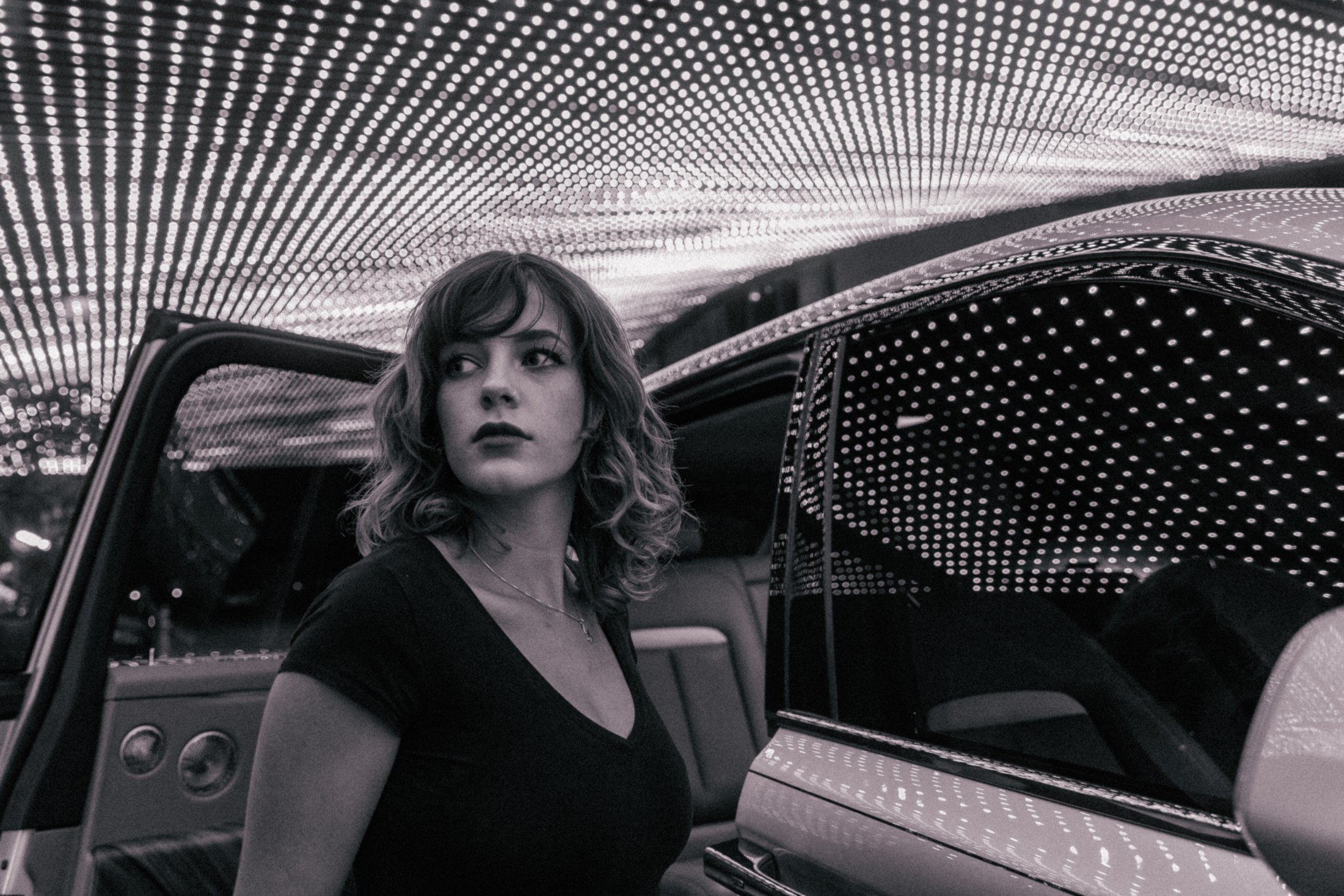 Rolls-Royce Cullinan – woman stepping out of the car under a ceiling of bulb lights, black and white, photo Jon Filin
