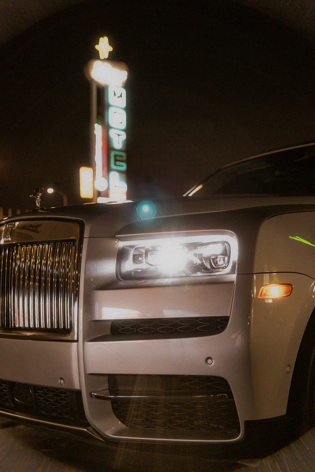 Rolls-Royce Cullinan – grille and lit headlight in front of a vintage motel neon sign, Los Angeles, photo Jon Filin